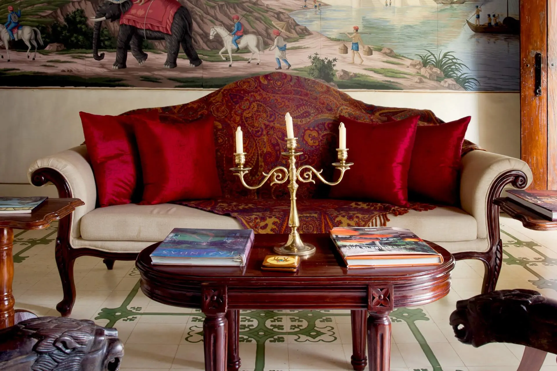 Antique sofa with red cushions behind an antique wooden table with golden candlestick in the hotel's lobby